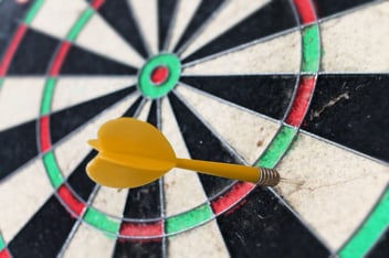 A dartboard with a dart stuck firmly outside the bullseye